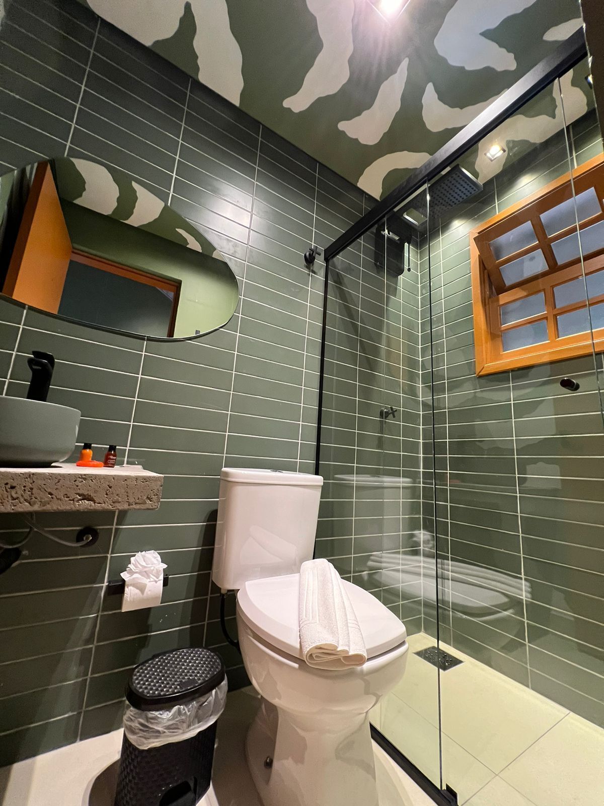A bathroom with a camouflage-patterned wall, a toilet, a sink, a mirror, and a shower area.