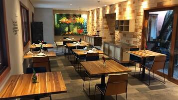 Restaurante con mesas y sillas de madera, un mural en la pared y una pared de piedra con una parrilla empotrada.