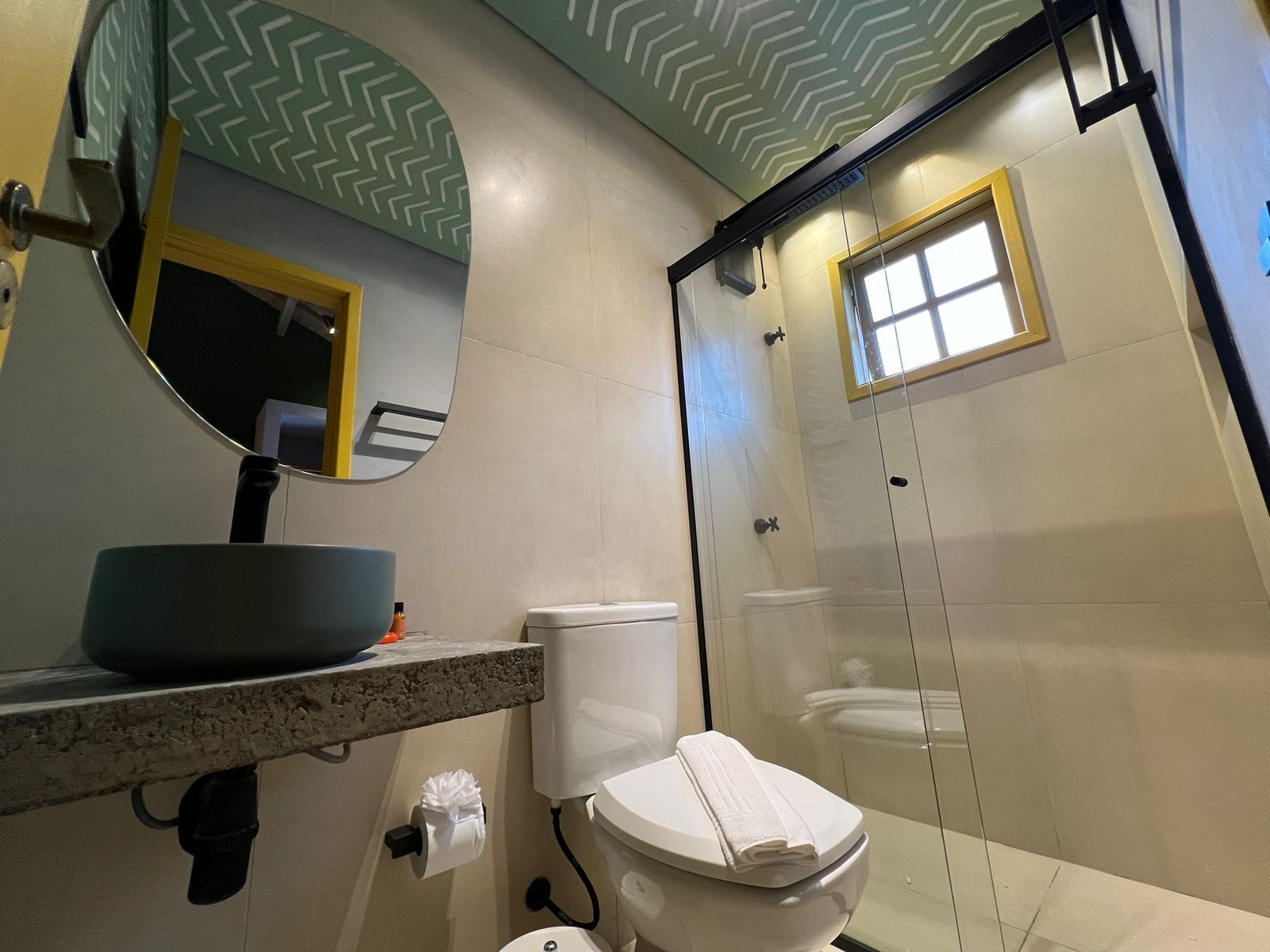 Ein Badezimmer mit rundem Spiegel, Toilette, Duschkabine und Waschbecken mit Ablagefläche.