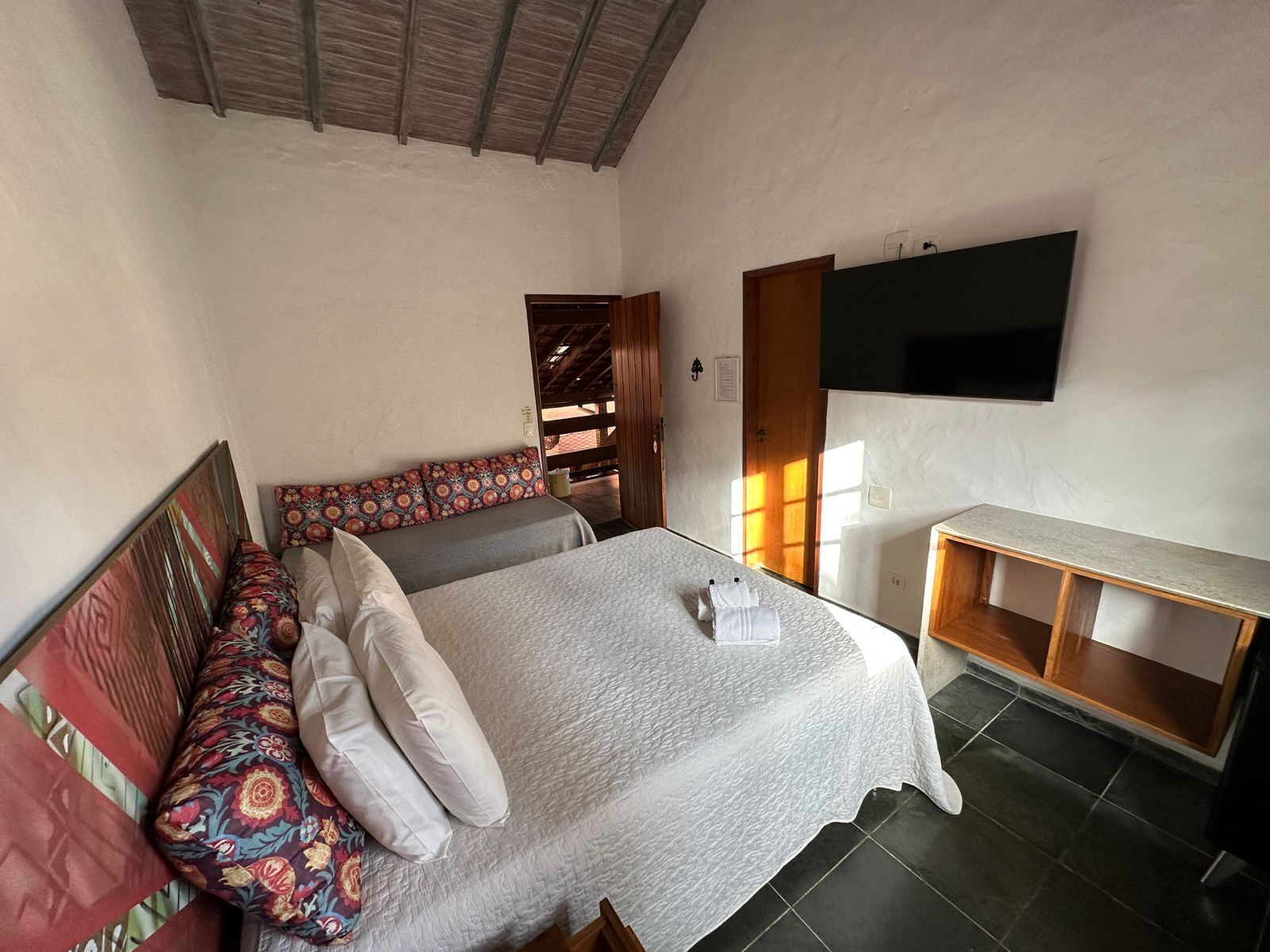 Un dormitorio con una cama, un banco con cojines, un televisor montado en la pared y otro banco de madera.