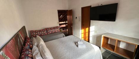 Un dormitorio con una cama, un banco con cojines, un televisor montado en la pared y otro banco de madera.