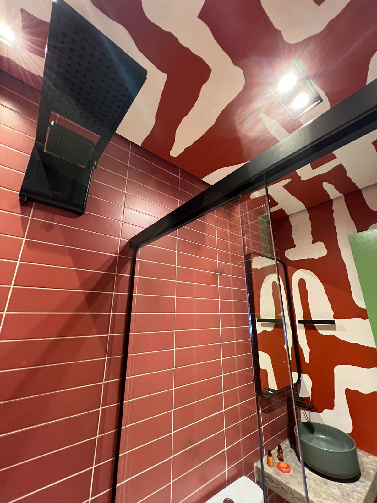 A bathroom with red and white patterned walls, a black shower seat, and a small sink with a green basin.