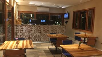 Un restaurante con mesas y sillas de madera, un muro decorativo y un televisor montado en la pared.