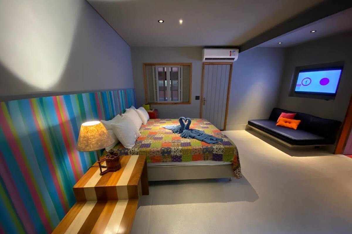 A bedroom with a bed, bedside table, lamp, and a TV on the wall.