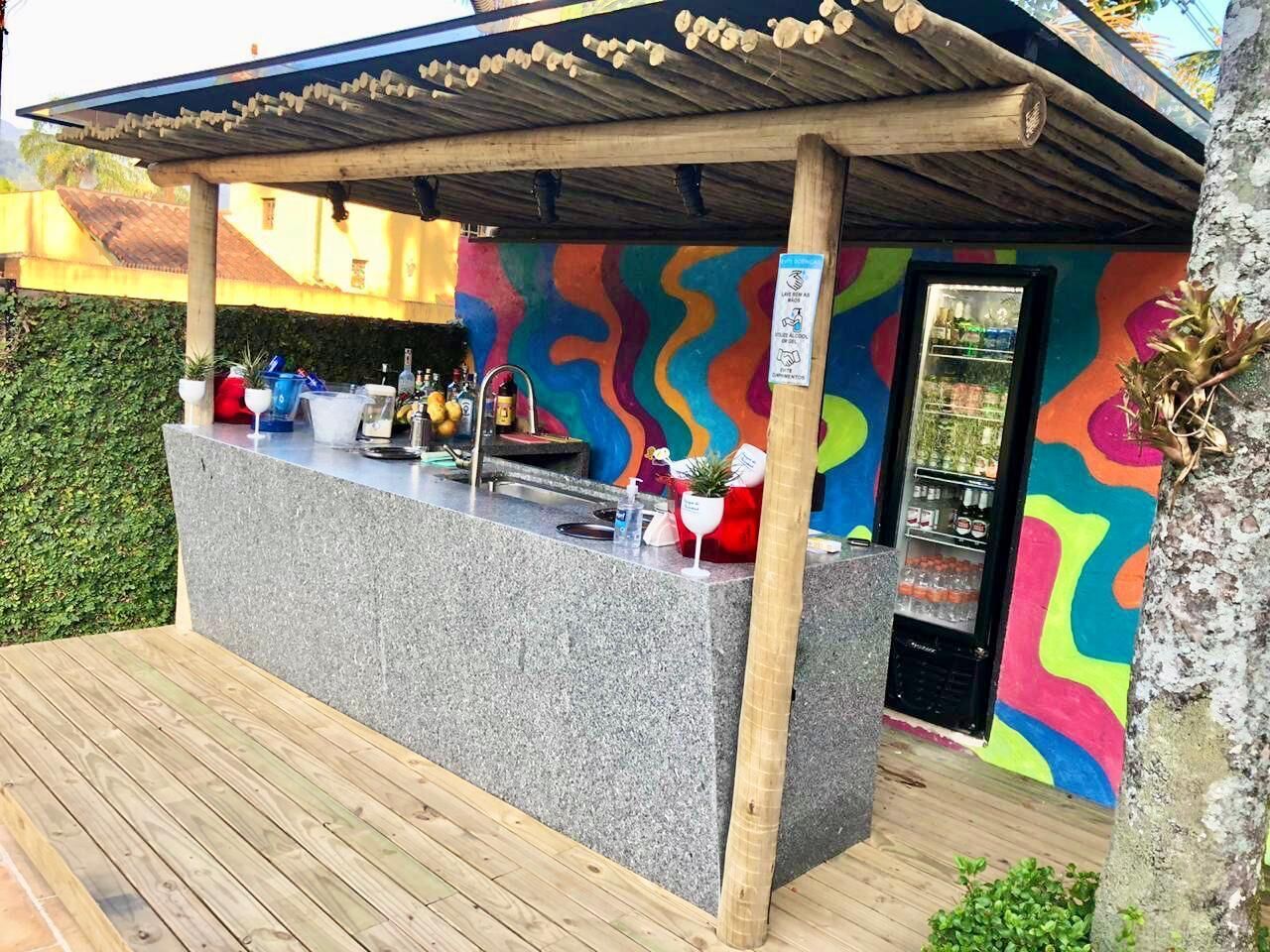 A tiki bar with a colorful mural, a counter with drinks, and a small refrigerator.