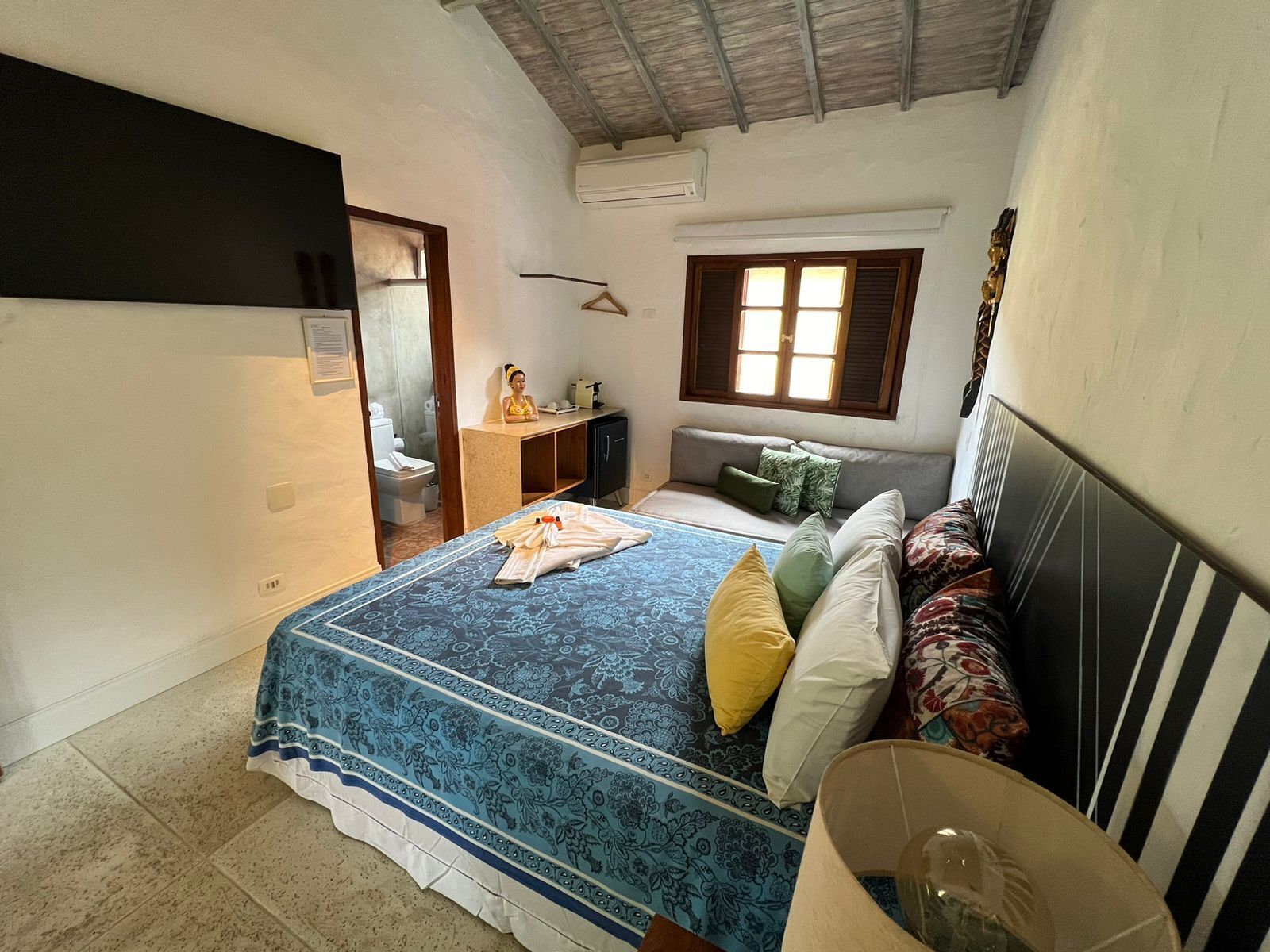 A bedroom with a bed, a bedside table, a hanging light fixture, and a window.
