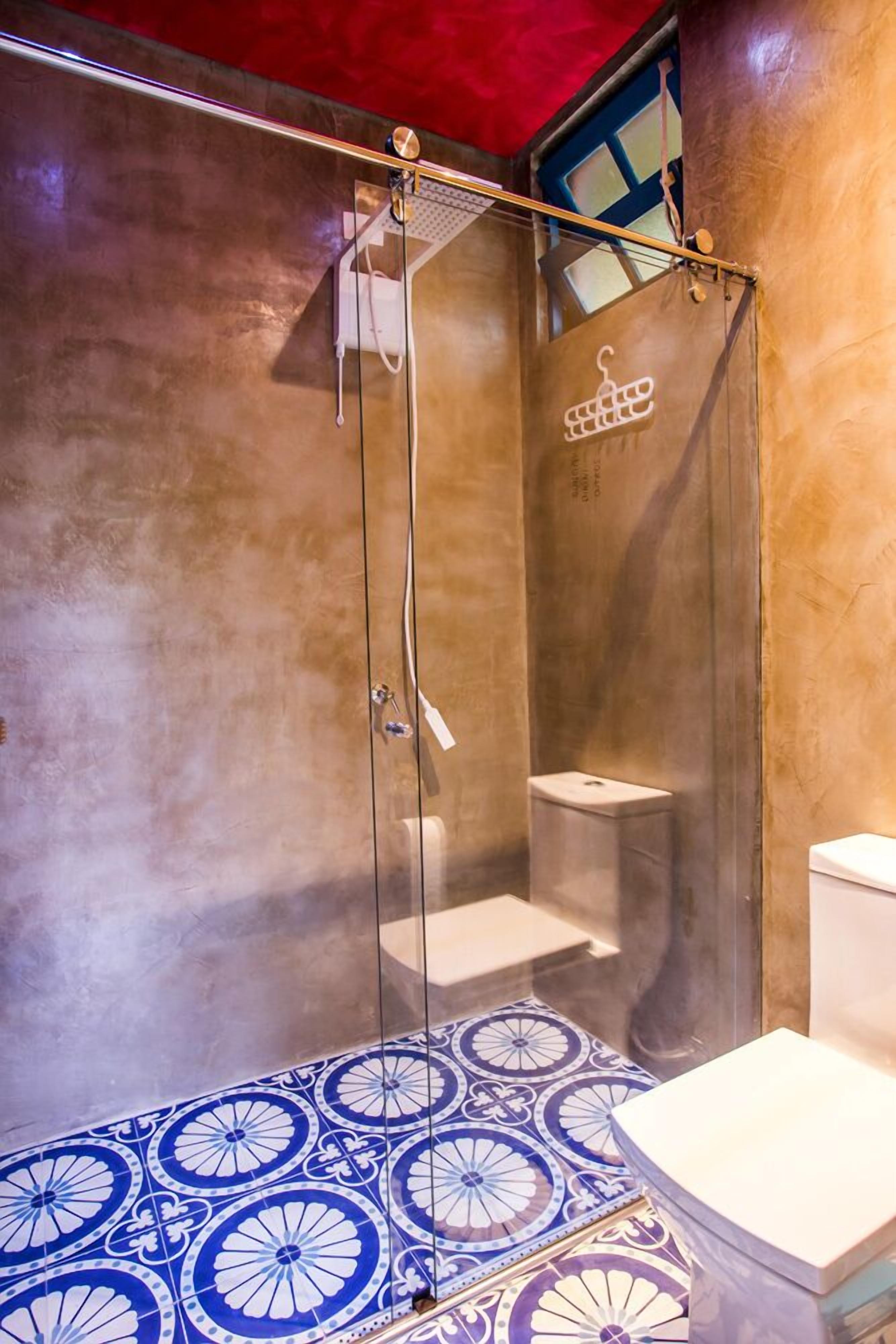 A shower with a glass door, a small sink, and a toilet in a bathroom with patterned tile flooring.