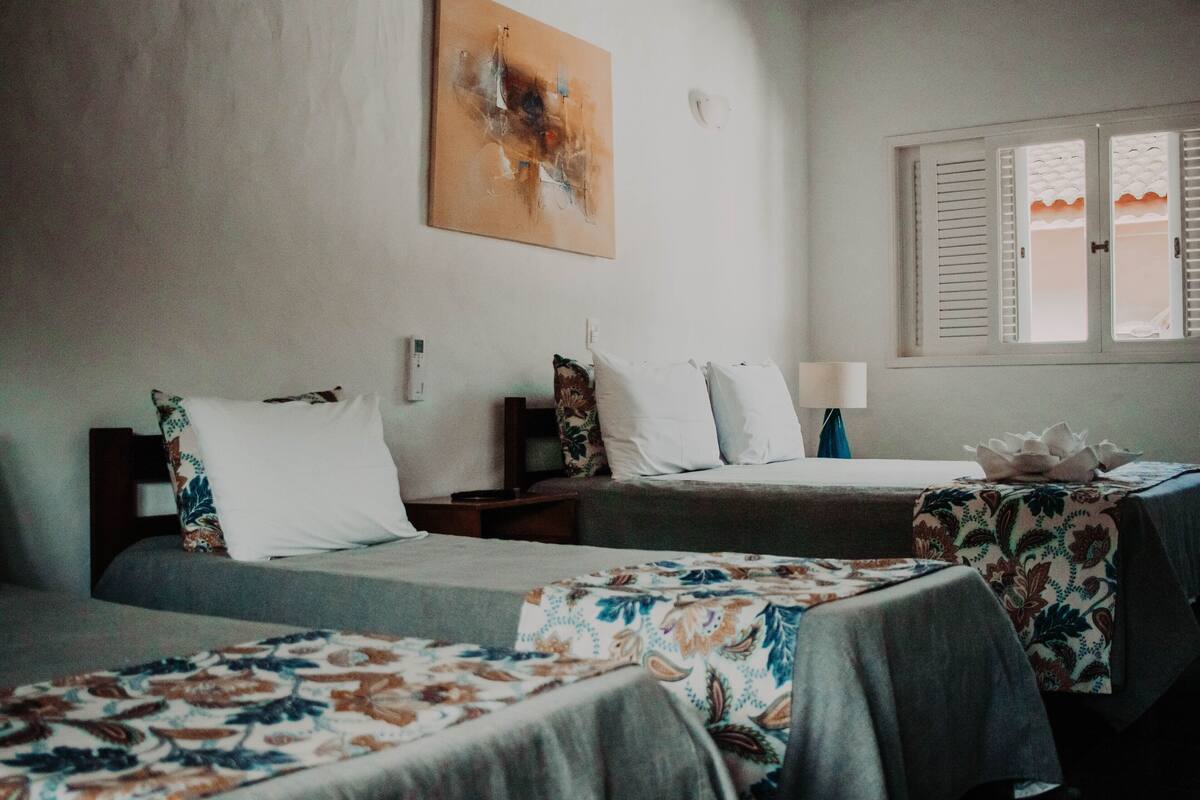 A hotel room with two beds, a nightstand, a lamp, and a window with shutters.