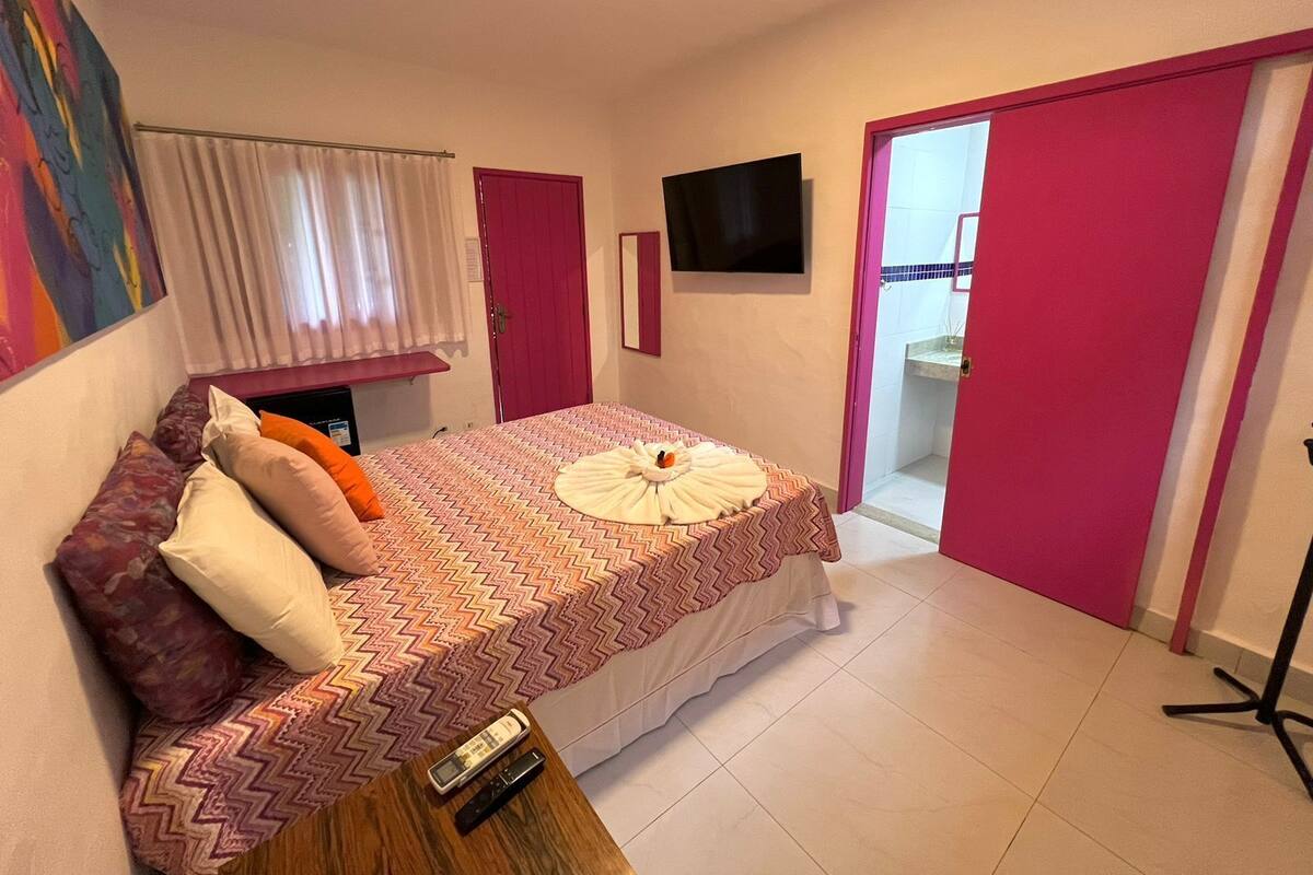 A bedroom with a bed, pillows, a TV, a bathroom door, and a shower area.