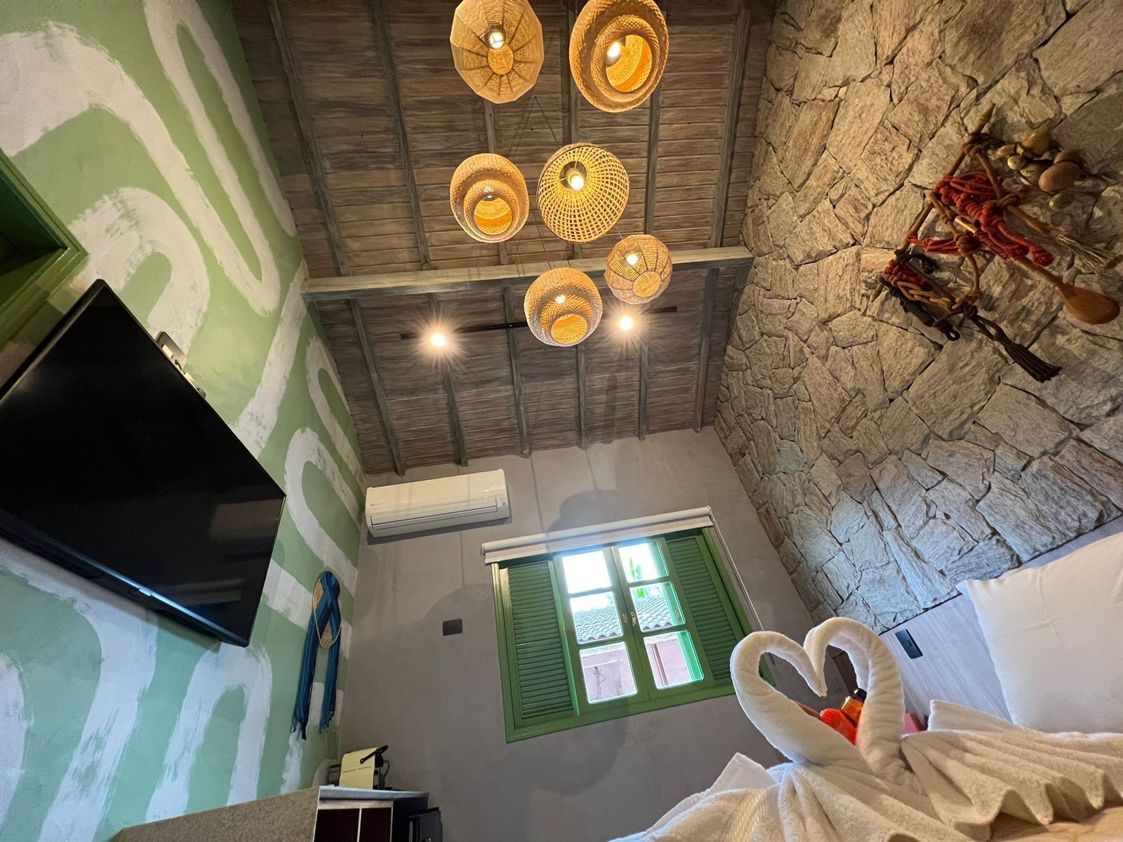 A room with a stone wall, a green window, a flat-screen TV, and a ceiling with woven light fixtures.
