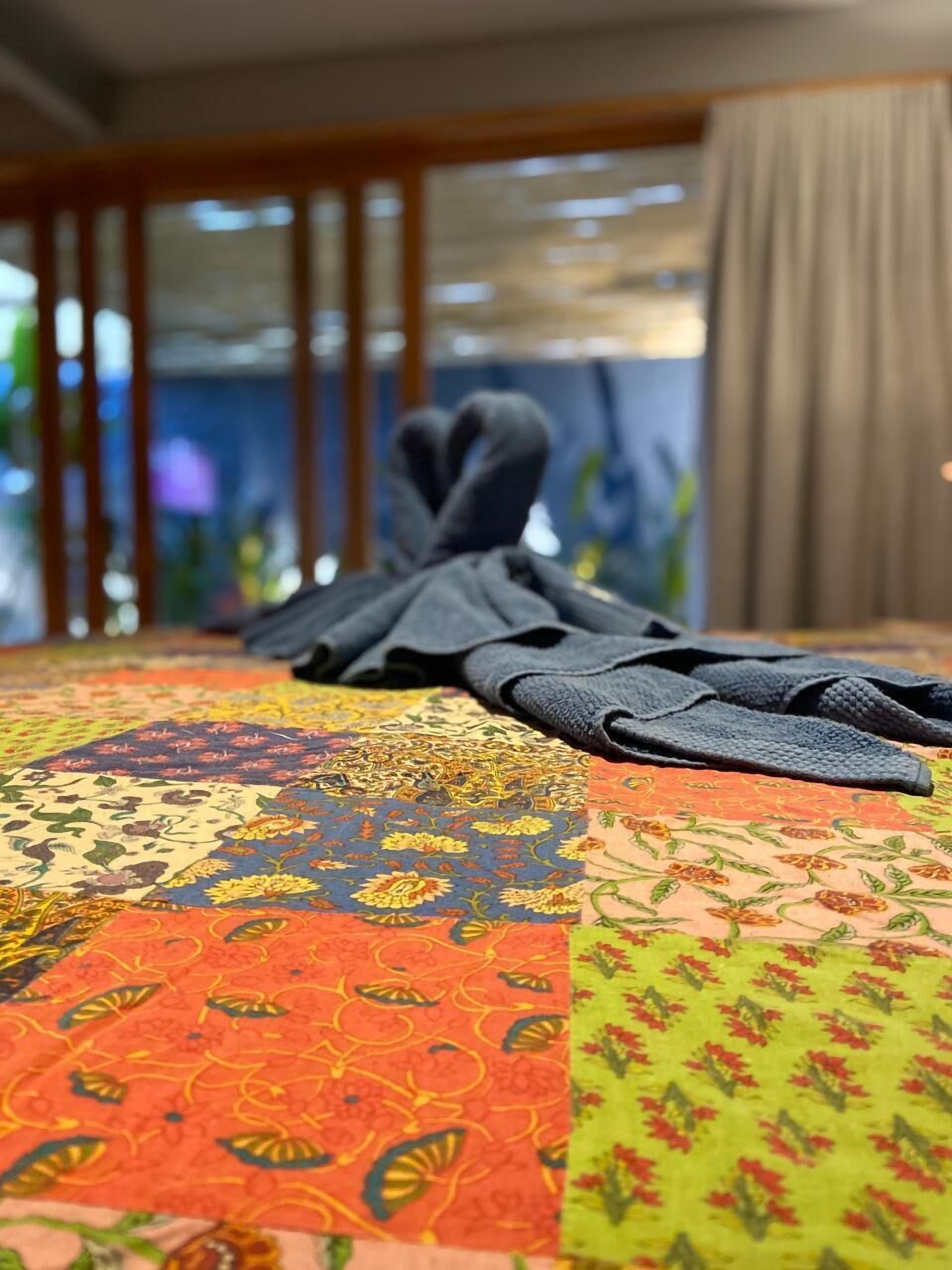A bed with a colorful, patterned bedspread and a dark, textured blanket.