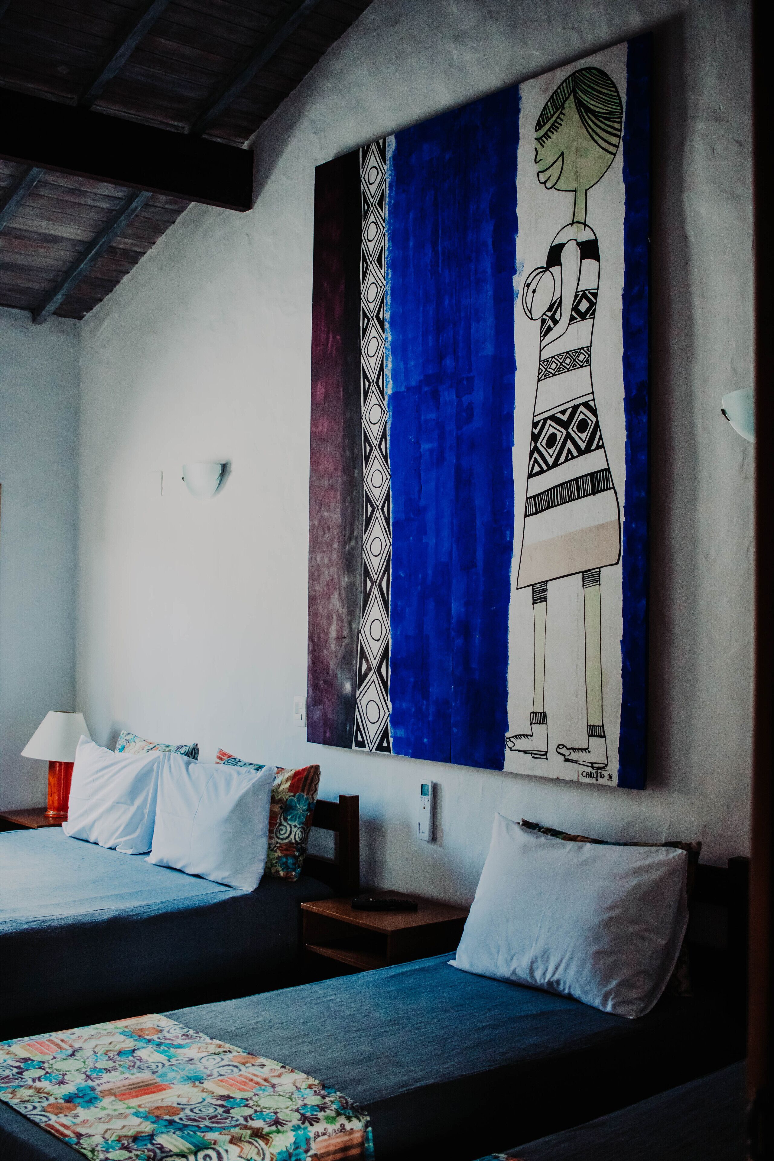Ein Zimmer mit zwei Betten, einem Wandbild und einem Nachttisch mit Lampe.