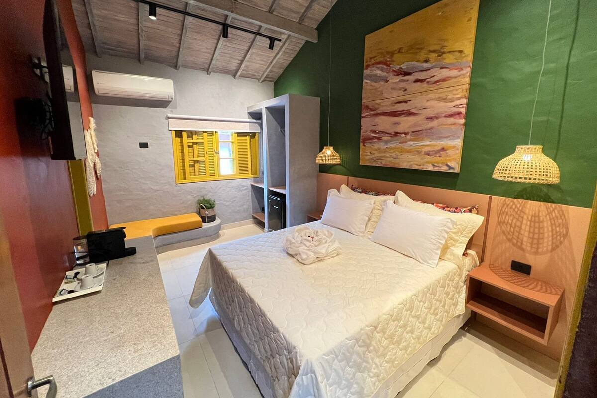 A modern bedroom with a large bed, a green accent wall, a painting, and a small bedside table.