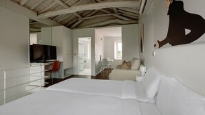 A bedroom with a large bed, a television, a desk with a chair, and a bathroom visible through an open door. - Olala Fine Arts Studios (Porto)