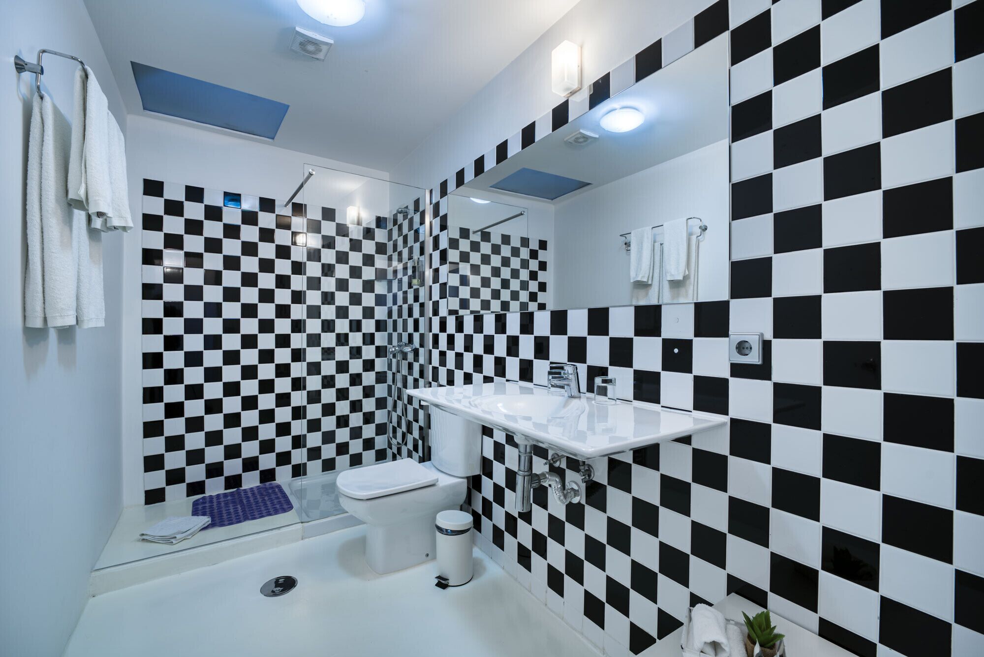 Une salle de bain moderne avec un mur recouvert de carreaux noirs et blancs formant un motif à carreaux, un lavabo blanc et une cabine de douche en verre.