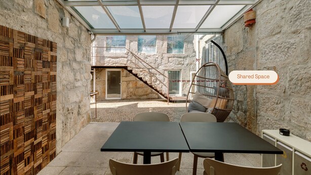 A modern interior with a glass ceiling, stone walls, a wooden wall panel, a hanging chair, and a table with chairs. - Olala Fine Arts Studios (Porto)