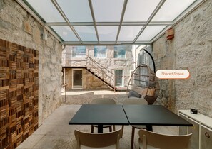 Un interior moderno con techo de vidrio, paredes de piedra, un panel de madera, un sillón colgante y una mesa con sillas.