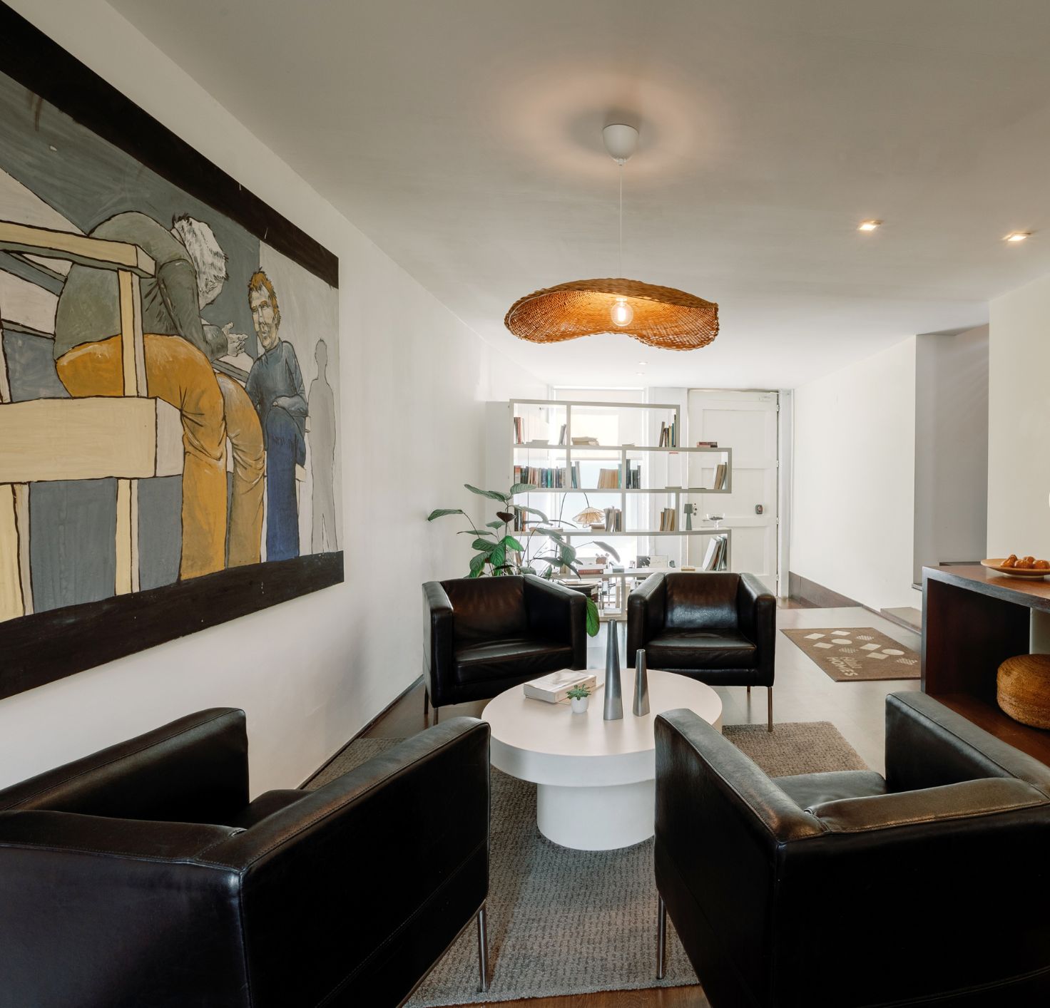 Una sala de estar moderna con una mesa redonda, sofás de cuero negro, una estantería y un cuadro grande en la pared.