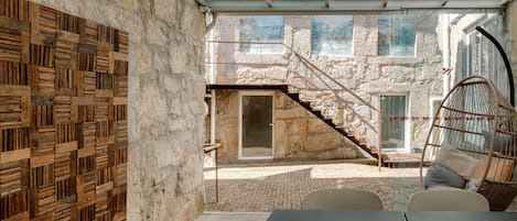 A modern interior with a glass ceiling, stone walls, a wooden wall panel, a hanging chair, and a table with chairs.