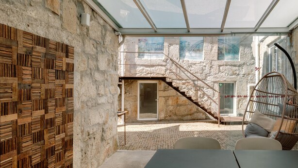 A modern interior with a glass ceiling, stone walls, a wooden wall panel, a hanging chair, and a table with chairs. - Olala Fine Arts Studios (Porto)