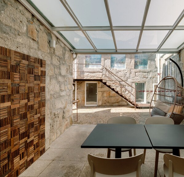 A modern interior with a glass ceiling, stone walls, a wooden wall panel, a hanging chair, and a table with chairs. - Olala Fine Arts Studios (Porto)