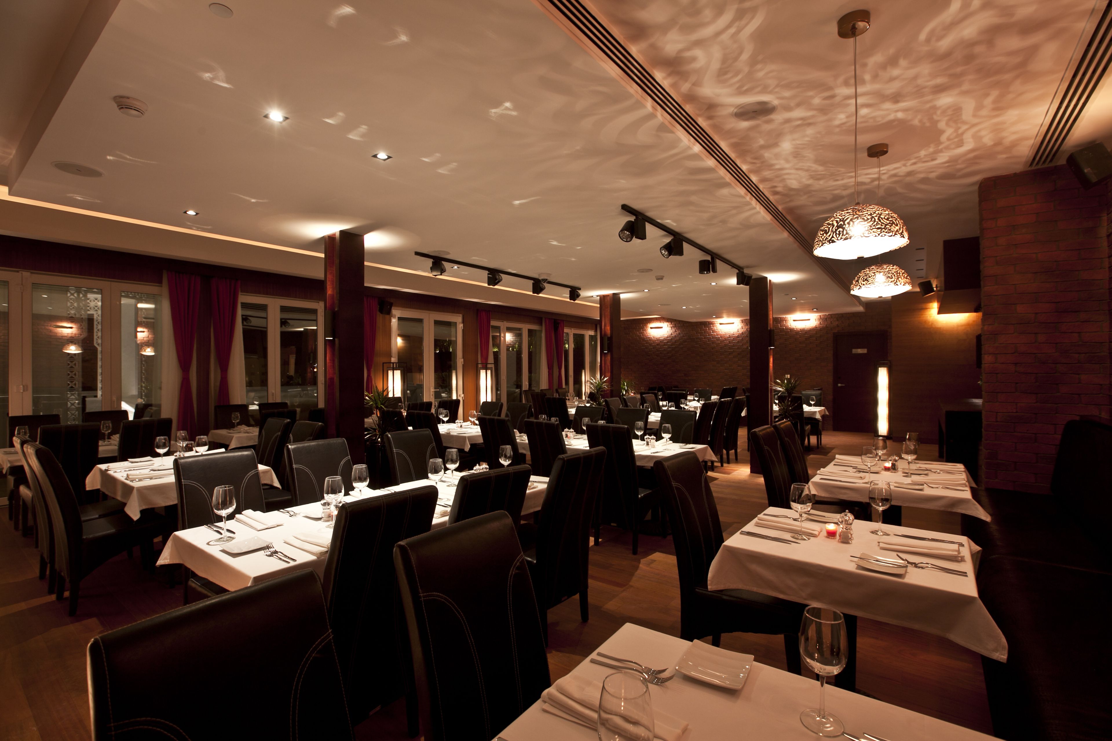 Un restaurante con varias mesas y sillas, iluminación en el techo y una pared de ladrillo.