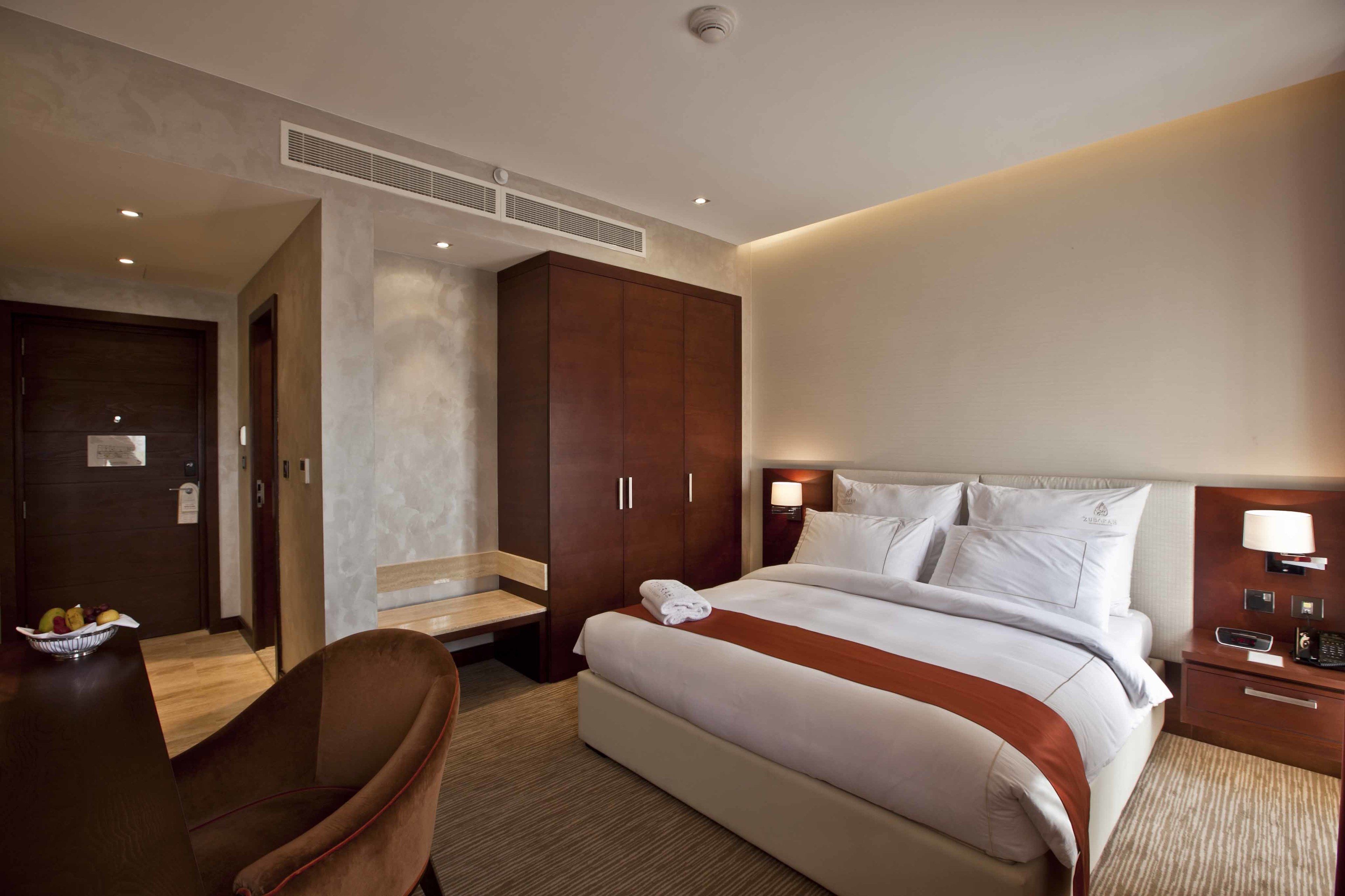 Ein Hotelzimmer mit einem großen Bett, einem Schreibtisch mit Stuhl, einem Kleiderschrank und einem Nachttisch mit Lampe.