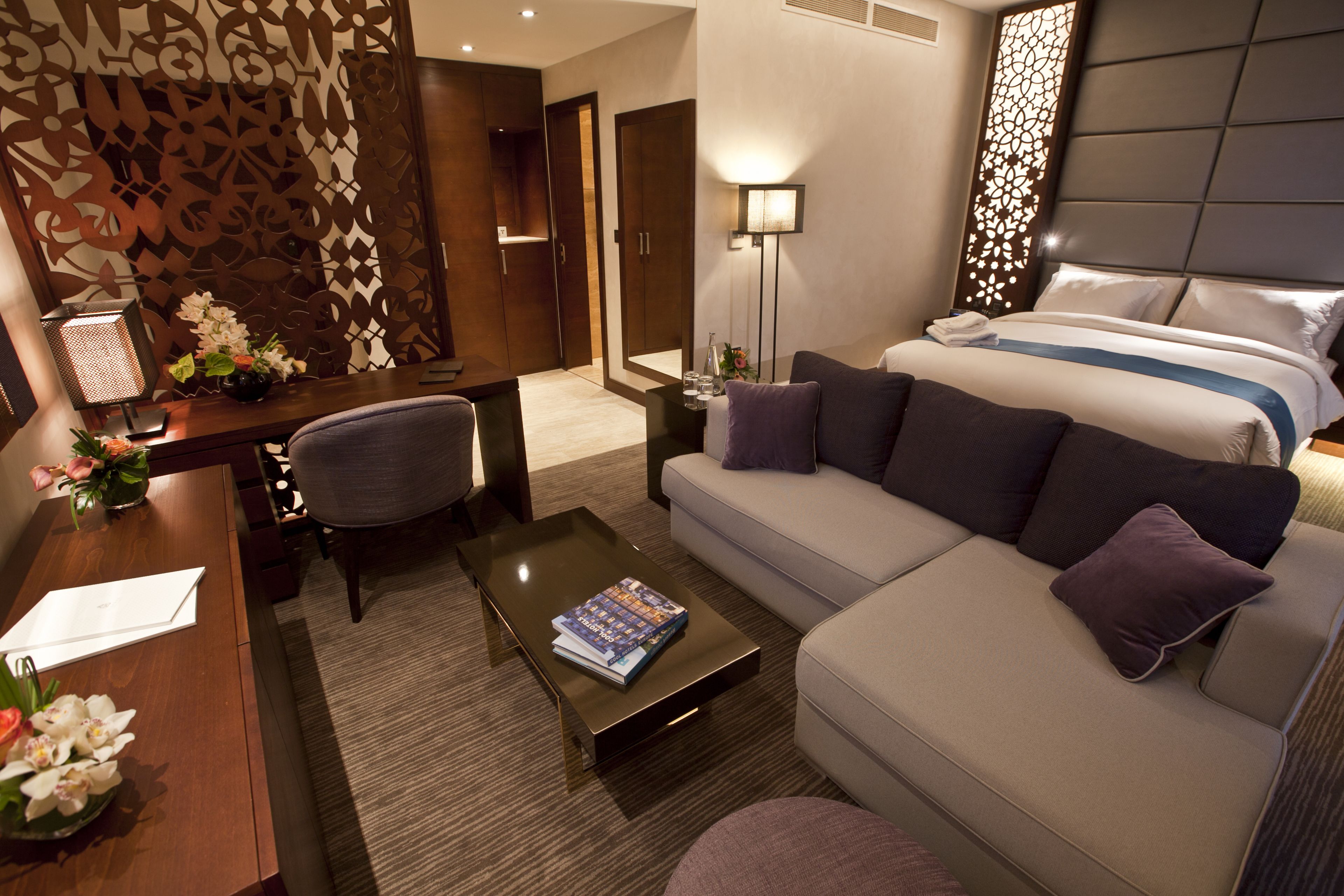 A modern hotel room with a sofa, a small table, a desk, and a bed.