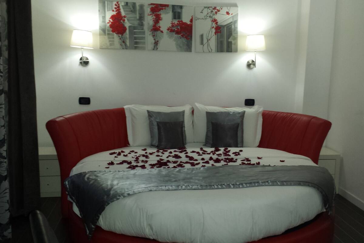 A bed with red and white bedding, two pillows, and rose petals scattered on it.