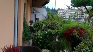 Un balcón con una mesa redonda y sillas, rodeado de plantas y flores en macetas.