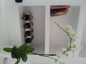 A white shelf with four wine bottles and a book. - Gregorio VII Luxury Suites (Rome)