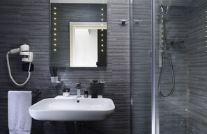 A modern bathroom with a white sink, a hairdryer, and a glass-enclosed shower. - Gregorio VII Luxury Suites (Rome)