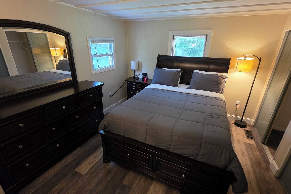 A bedroom with a bed, dresser, mirror, bedside lamps, and windows.