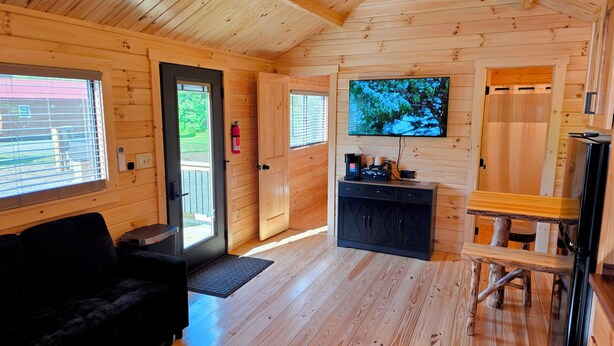 A wooden cabin interior with a sofa, a coffee station, a television, and a door leading outside. - Abbot Trailside Lodging (Abbot)
