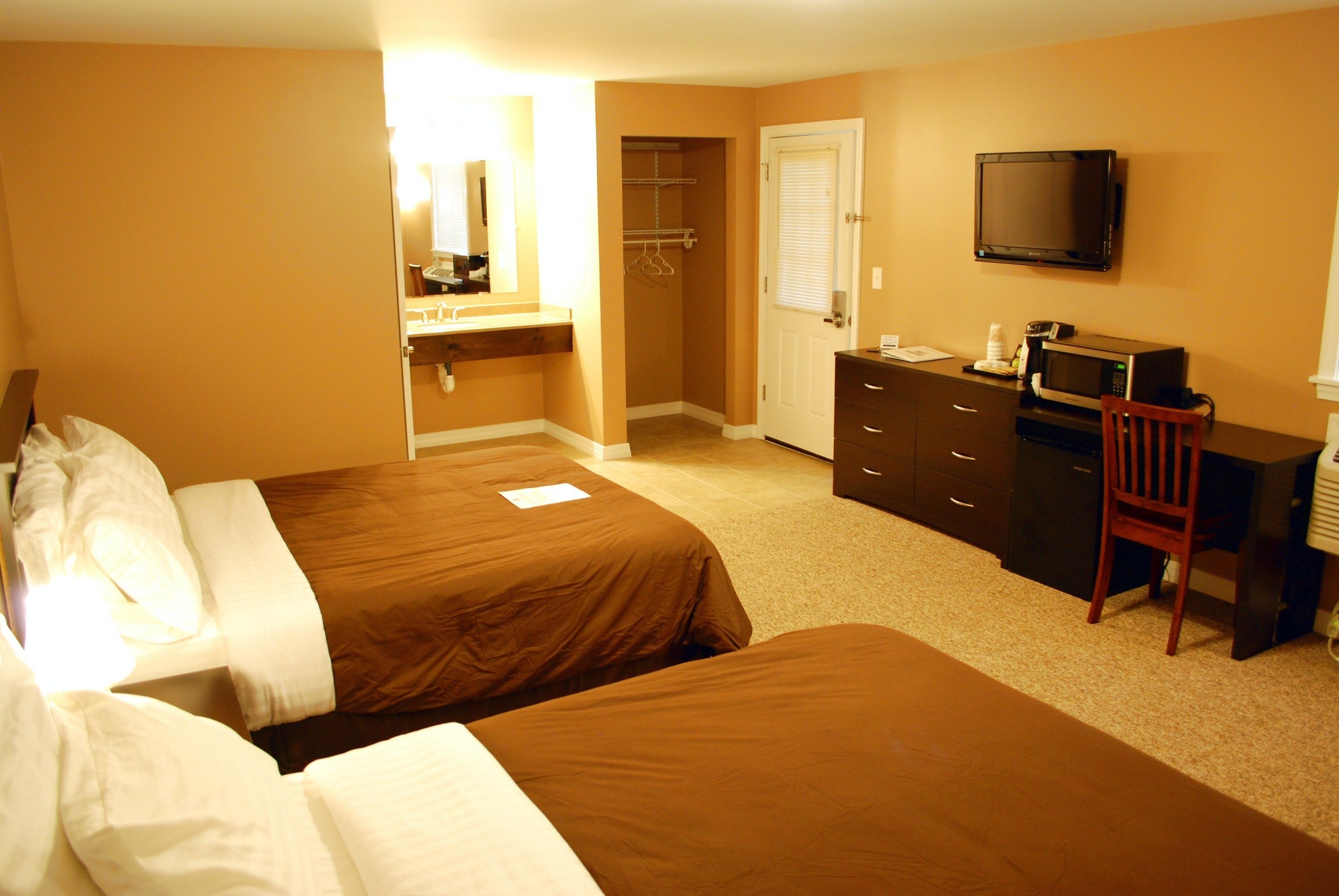 A hotel room with two beds, a desk with a chair, a television, a microwave, and a closet.