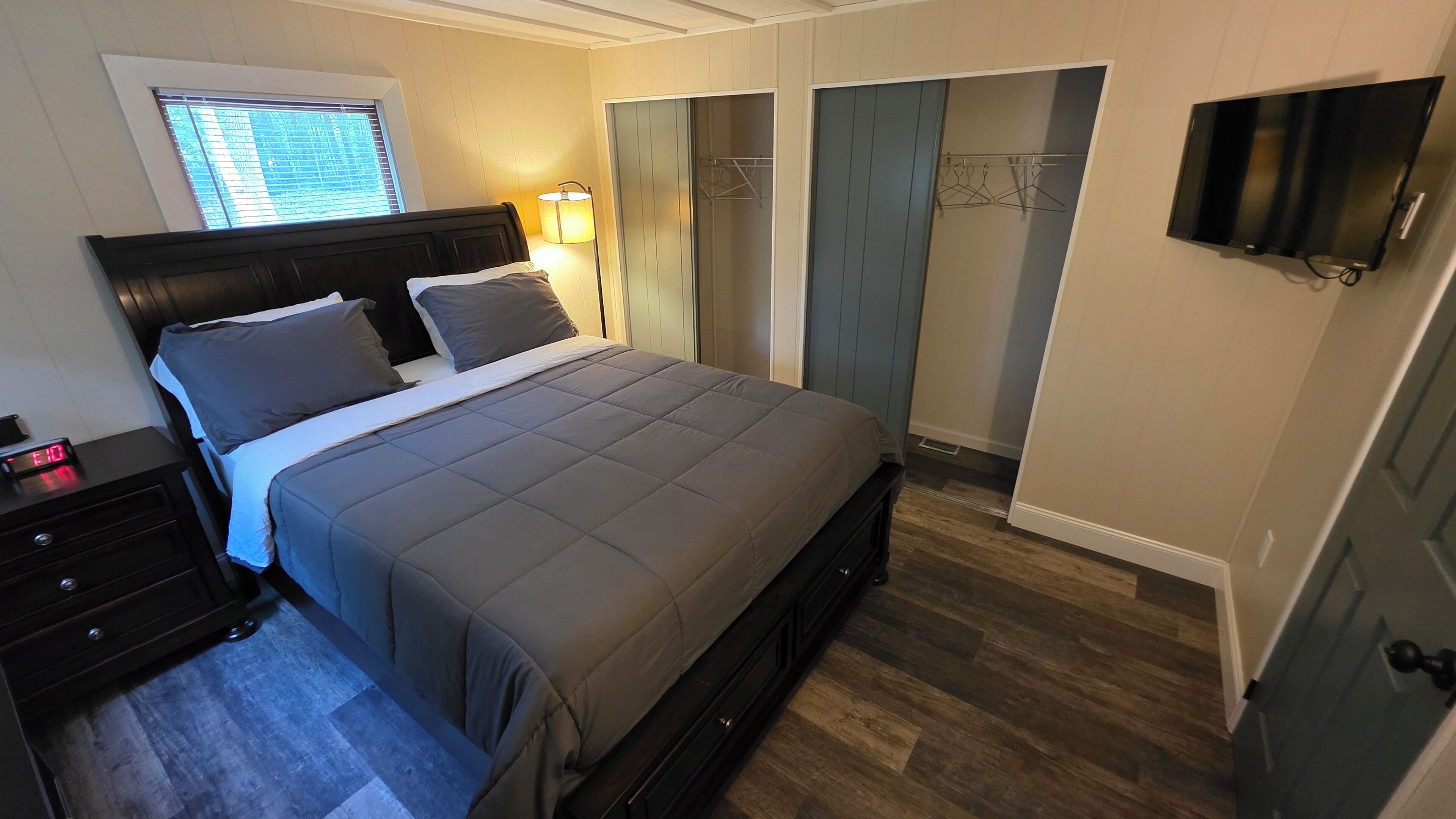 Un dormitorio con cama, mesita de noche, lámpara, armario y televisor.