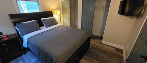 Un dormitorio con cama, mesita de noche, lámpara, armario y televisor.