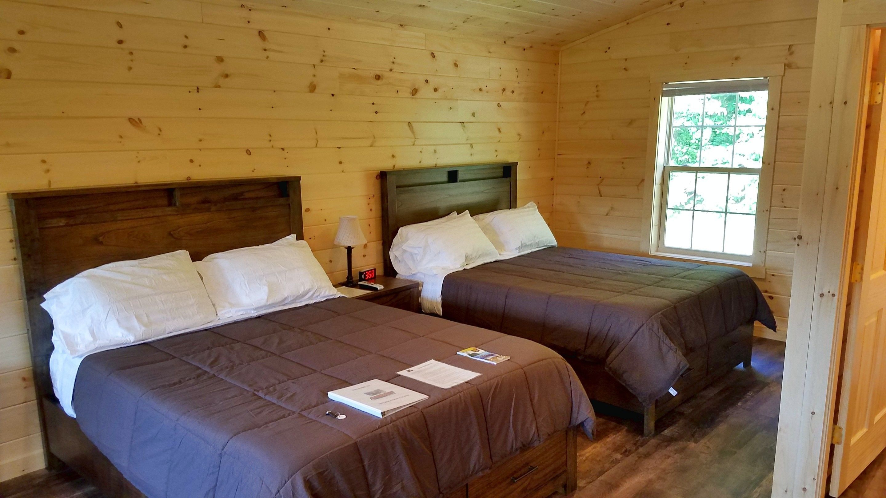 Une chambre dans un chalet en bois, avec deux lits, une table de chevet et une fenêtre.