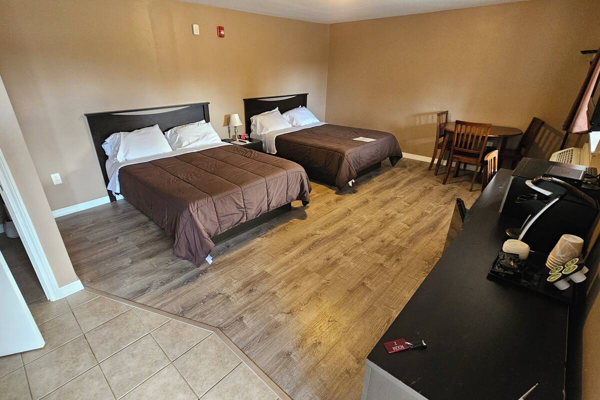A hotel room with two beds, a desk, a chair, and a TV.
