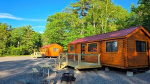 Two wooden cabins with metal roofs, a picnic table, and a fire pit in a forest setting. - Abbot Trailside Lodging (Abbot)