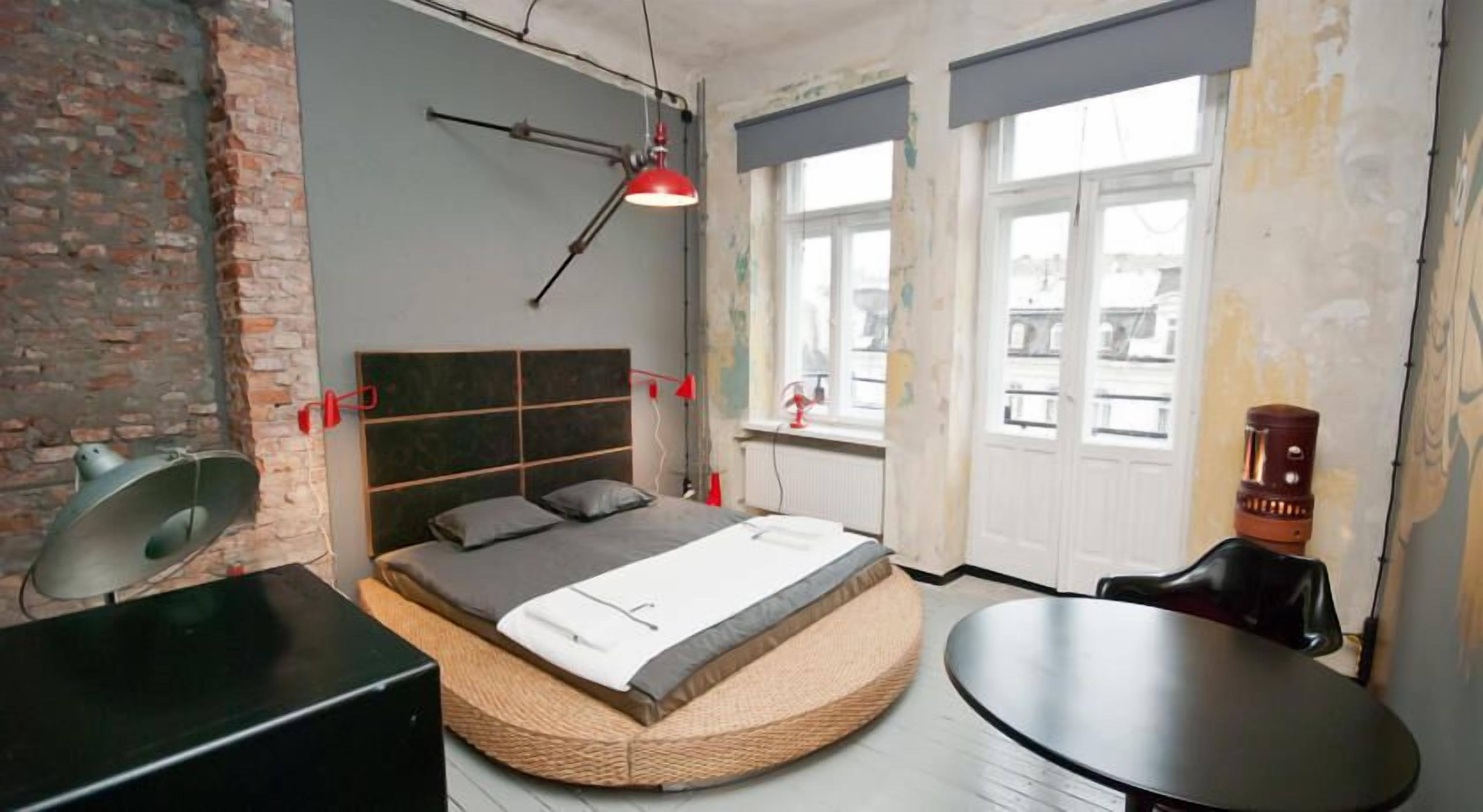 A bedroom with a bed, a round table, a lamp, and a brick wall.