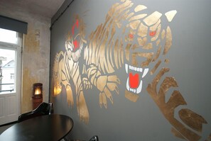 A room with a large tiger mural on the wall, a table, and a chair. - Lofthotel Sen Pszczoły (Warsaw)