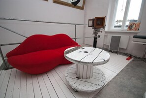A room with a red bean bag chair, a white table with a wooden top, and a window with a view of buildings. - Lofthotel Sen Pszczoły (Warsaw)