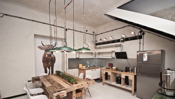 A modern kitchen with a wooden dining table, white chairs, a sink, a refrigerator, and a wall-mounted TV. - Lofthotel Sen Pszczoły (Warsaw)