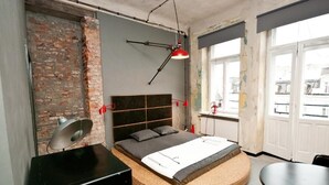 A modern bedroom with a brick wall, a round bed with a woven base, a desk, and a dining table. - Lofthotel Sen Pszczoły (Warsaw)