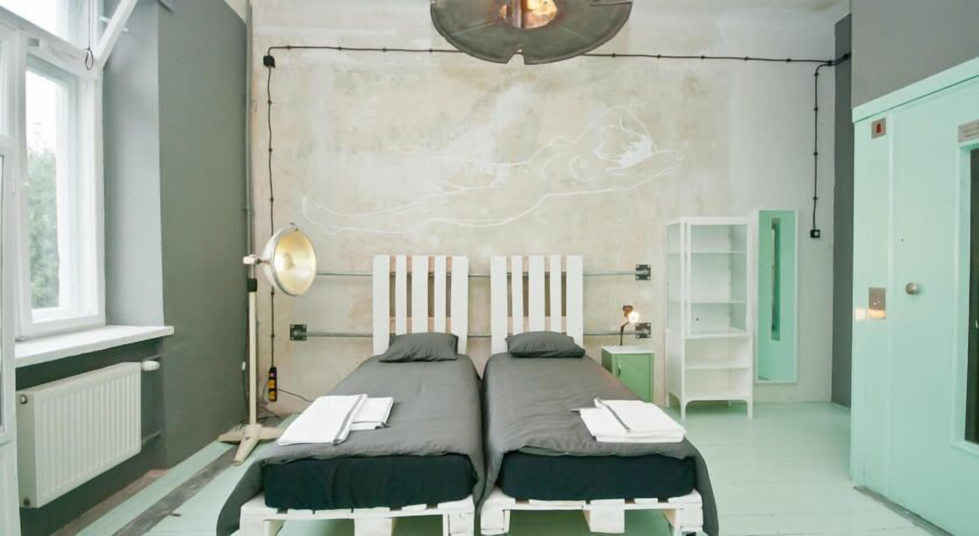 Une chambre avec deux lits, une fenêtre, un radiateur, une lampe et une porte verte.