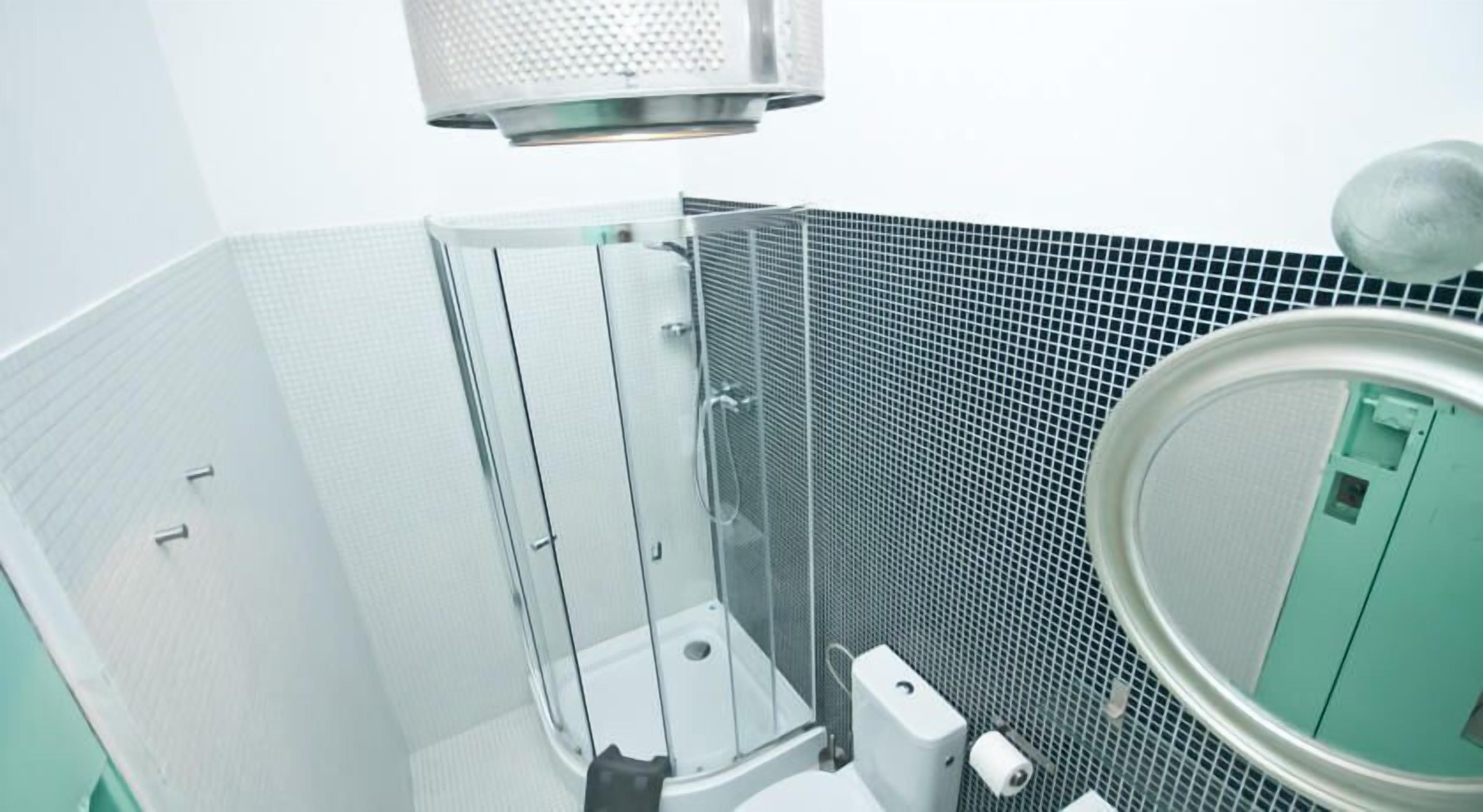 Un baño con cabina de ducha de vidrio, pared con azulejos y inodoro verde.