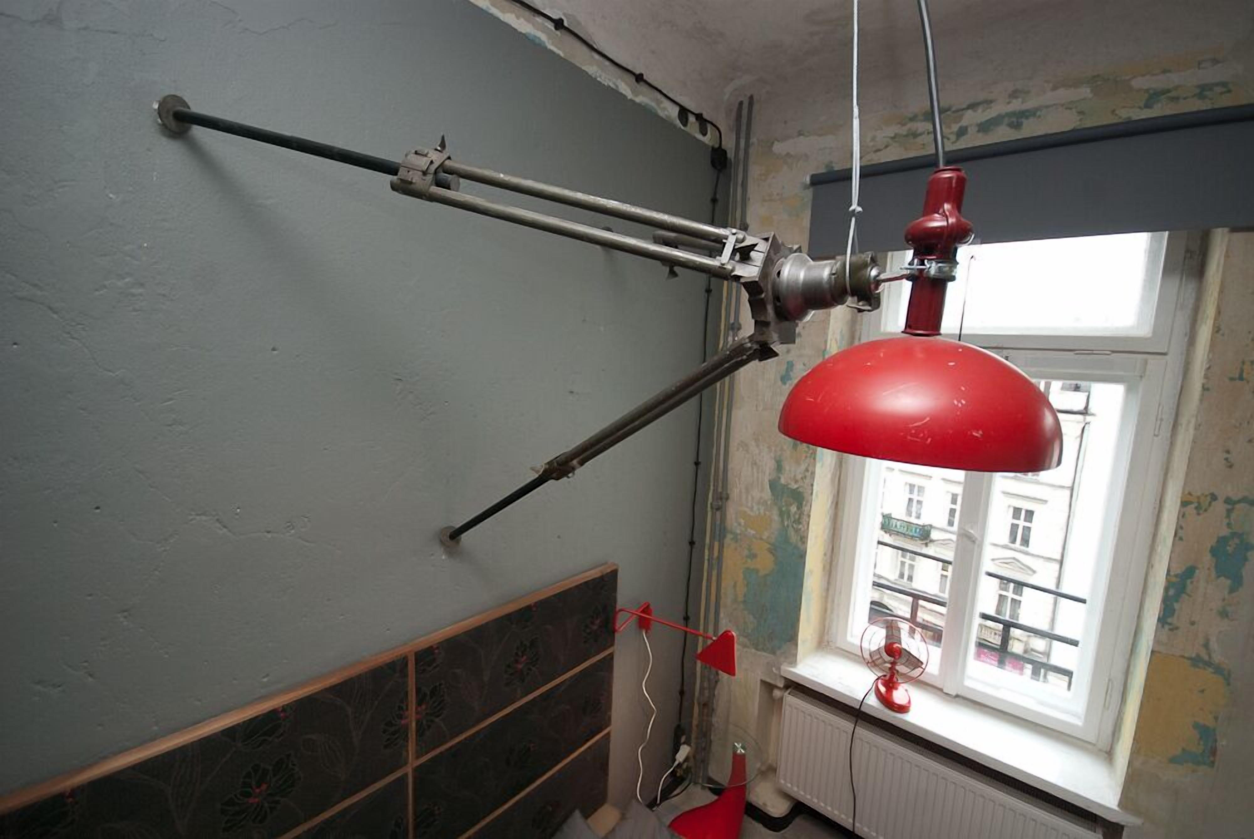 A room with a red hanging lamp, a radiator, and a window with a view of buildings.