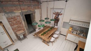 A rustic kitchen with a wooden table, hanging green lights, and a cow decoration. - Lofthotel Sen Pszczoły (Warsaw)