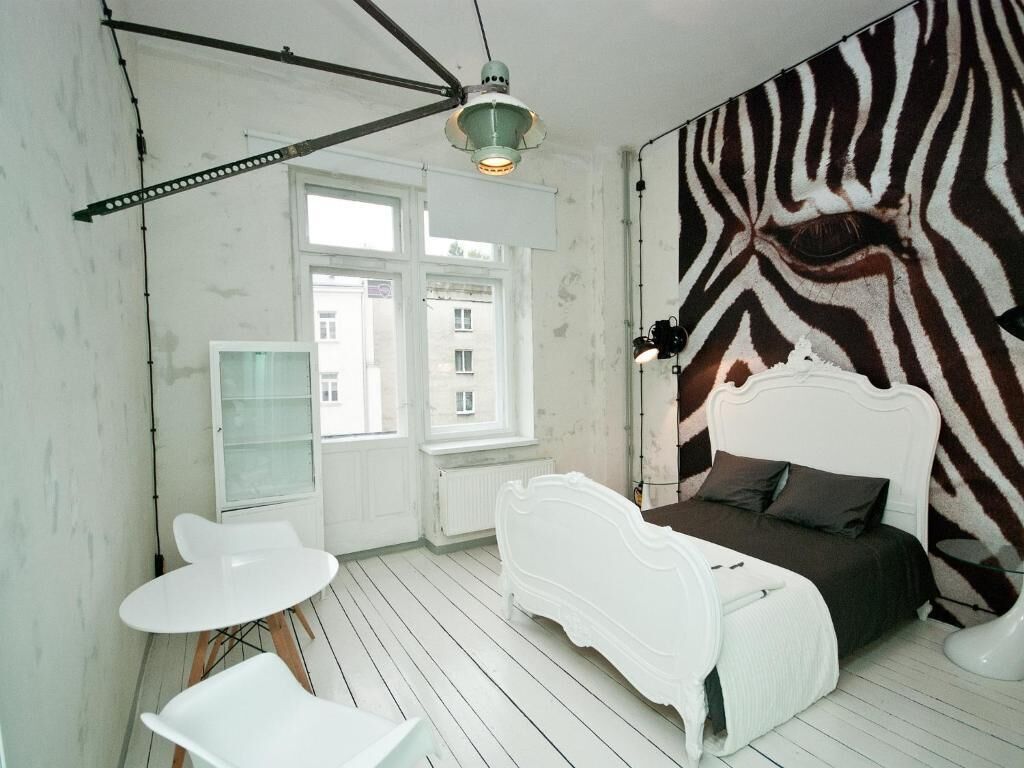Ett rum med en vägg som har zebrasträcksmönster, en vit säng, ett vitt bord och en vit stol.